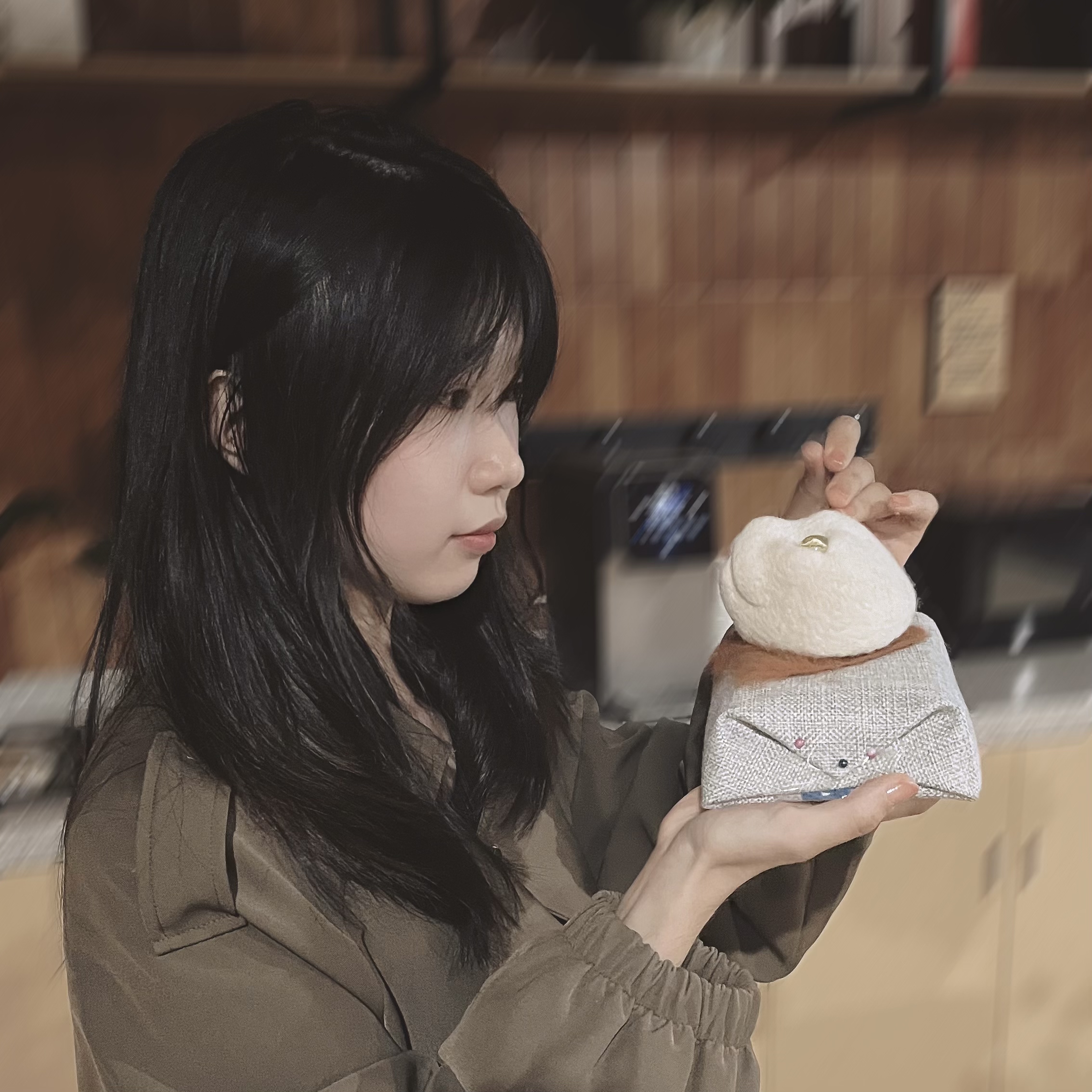 A woman with long dark hair is carefully working on a wool felt sculpture of a cat's head, focusing on the details.