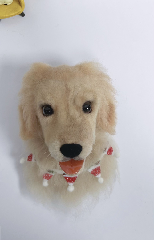 A wool felt sculpture of a golden retriever's head with lifelike eyes and a festive garland around its neck.